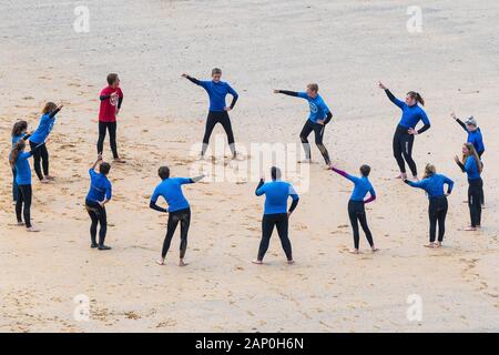 Les surfeurs débutants l'échauffement avant une leçon de surf sur la grande plage de l'Ouest à Newquay en Cornouailles. Banque D'Images