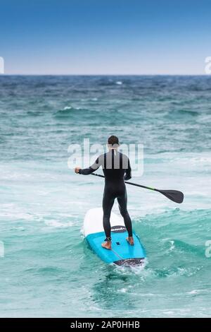 Un stand up paddle boarder de partir à la mer à Newquay dans Fistral à Cornwall. Banque D'Images