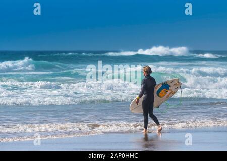 Un homme surfer carrying his surfboard et regardant la mer à Newquay dans Fistral à Cornwall. Banque D'Images