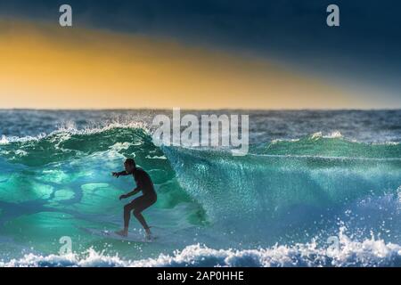 Un surfer une vague par le contre-jour coucher de soleil à Newquay dans Fistral à Cornwall. Banque D'Images