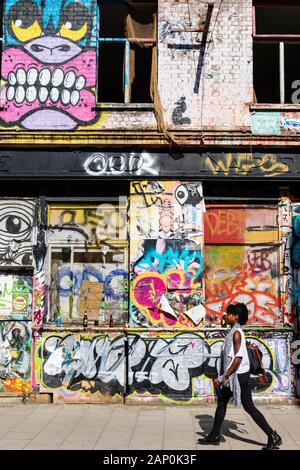 Une jeune femme marche dernières graffitis colorés couvrant le Seigneur Napier une pub à Hackney Wick. Banque D'Images