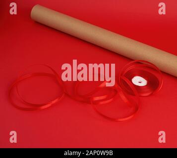 Rouleau de papier brun d'emballage, d'une bobine de ruban rouge et un cadeau enveloppé dans du papier kraft brun sur un fond rouge, faisant de surprises Banque D'Images