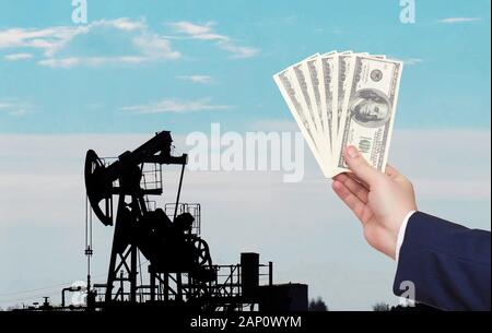 Un homme détient l'argent dollars dans sa main dans le contexte d'un puits qui produit du pétrole et du gaz. Le concept de l'économie pétrolière et la hausse de prix Banque D'Images