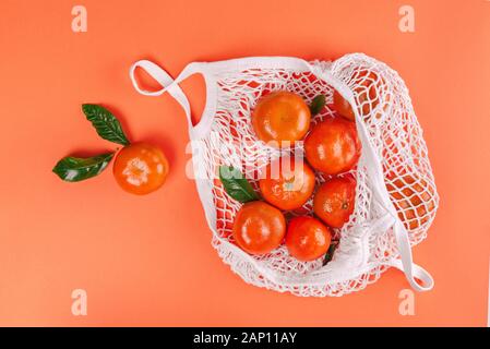 Mandarines frais mûrs avec des feuilles vertes en sac-filet de coton blanc sur fond orange. Mise à plat, vue du dessus, copiez l'espace. Banque D'Images