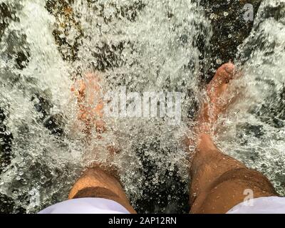 Le pied des deux pieds qui se trouvent dans la cascade qui coule JusQu'À ce que l'eau se scinde en granules Banque D'Images