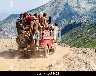 Les gens s'accrochent à une jeep surchargée, conduisant sur la route poussiéreuse jusqu'au col de Babusar Banque D'Images