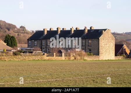 Une série de Yorkshire typique construite en pierre des maisons mitoyennes avec cheminées à côté d'un champ d'herbe à Huddersfield, West Yorkshire, Royaume-Uni Banque D'Images