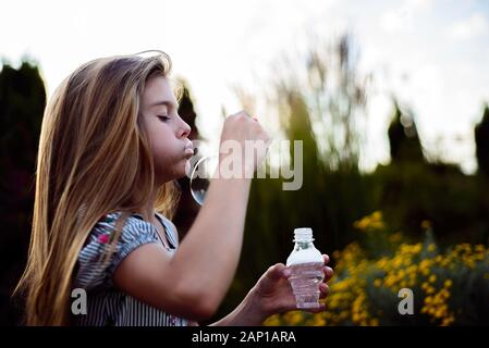 Portrait d'une belle petite fille soufflant des bulles de savon. Un enfant joue avec des bulles, sur un fond vert. Piscine Banque D'Images