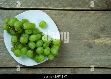 Raisins blancs sur une plaque blanche. La plaque est sur un sol en bois. Vue de dessus Banque D'Images