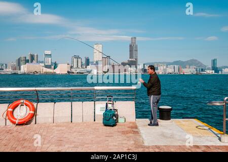 Hong Kong, Chine - Novembre 2019 : Fisher man avec la canne à pêche sur la côte avec HongKong skyline en arrière-plan Banque D'Images