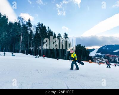 Homme avec snowboard à red christmas hat walking up par neigé hill Banque D'Images