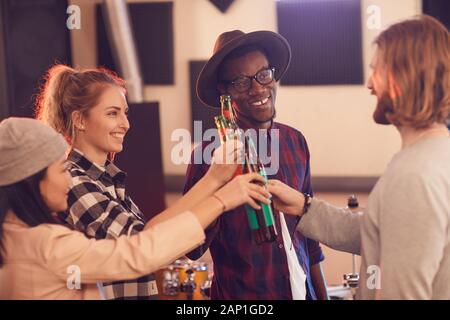 Groupe multi-ethnique des jeunes le grillage avec les bouteilles de bière tout en profitant de répétition en studio de musique Banque D'Images