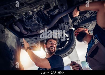 De nombreux mécaniciens examinent la voiture et discutent de la réparation en service automobile. Banque D'Images