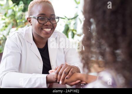 Black woman doctor smiling holding patient mexicain part mixed race jeunes au bureau de médecins Banque D'Images
