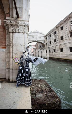 Une personne dans le masque de carnaval penchant contre un mur d'un bâtiment avec le pont de soupirs dans l'arrière-plan Venise Italie Banque D'Images