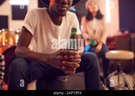 La mi-section portrait of trendy African man holding Beer bottle tout en vous relaxant dans Music Studio Banque D'Images