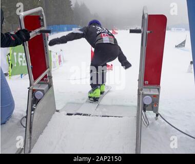 Coupe du monde de snowboard 2020 Rogla, en Slovénie. Un concurrent au moment de quitter le portail de démarrage et l'accélération commence en bas de la piste. Banque D'Images