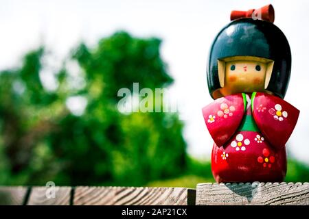 Boites japonaises Kokeshi Doll vêtu de kimono traditionnel, peints à la main en rouge et fleuris avec jardin vert en arrière-plan Banque D'Images