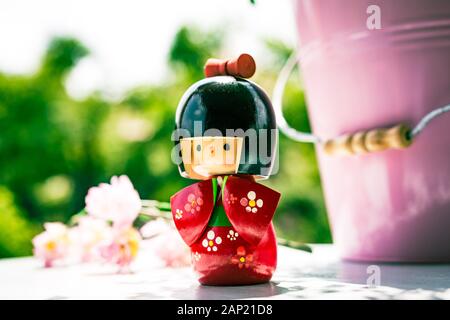 Japonais Kokeshi Doll vêtu de kimono traditionnel, peint à la main en rouge et en fleurs. Fleurs roses de cerisier à l'arrière-plan Banque D'Images