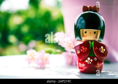 Japonais Kokeshi Doll vêtu de kimono traditionnel, peint à la main en rouge et en fleurs. Fleurs roses de cerisier à l'arrière-plan Banque D'Images