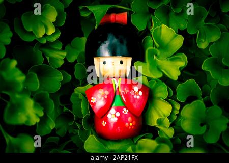 Bois japonais Kokeshi Doll vêtu de kimono traditionnel sur les feuilles de ginkgo biloba arrière-plan, peint à la main en rouge et florals Banque D'Images