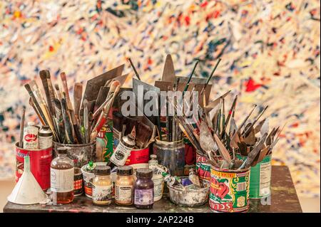 Une variété de pinceaux et de la peinture dans un assortiment habituel de conteneurs en face d'une toile d'artiste dans son atelier Banque D'Images