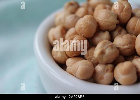 Vue rapprochée d'un bol blanc rempli de pois chiches (Cicer arietinum), sur une table en bois avec tapis de table vert menthe. Avec copyspace. Banque D'Images