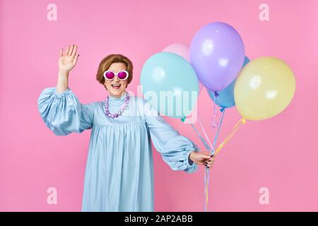 Jolie vieille femme avec des ballons en costume bleu disco dancer. Animateur de fêtes d'enfants, clown drôle sur fond rose Banque D'Images