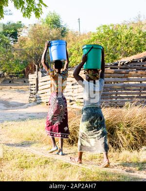 Deux femmes malawiennes marchent vers leur village depuis le puits avec un seau d'eau en plastique sur leurs têtes Banque D'Images