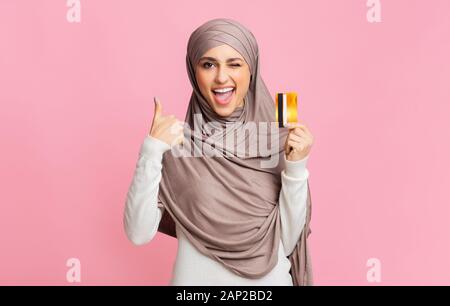 Femme musulmane dans hijab holding credit card et showing thumb up Banque D'Images