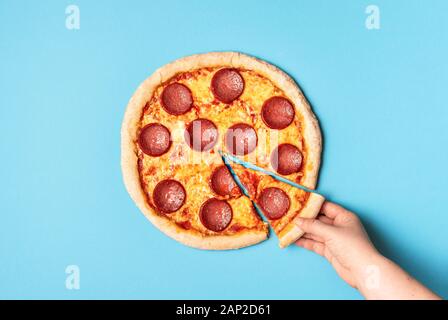 Femme prenant une tranche de pizza salami sur un fond bleu. Voir ci-dessus de pizza au pepperoni et une main attrapant une pizza slice. Le fast food. La nourriture bonne. Banque D'Images