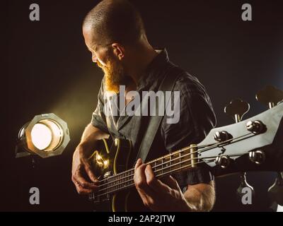 Photo d'un homme barbu jouant de la guitare électrique sur scène devant des spots. Banque D'Images