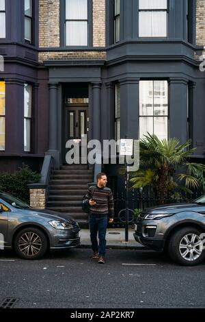 Jeune homme de quitter sa maison et à l'aide de son smart mobile aux maisons colorées sur Portobello Street dans le quartier de Notting Hill Banque D'Images