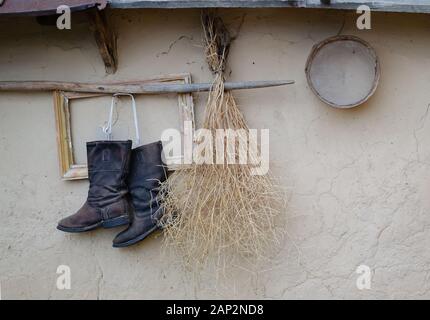 paire de chaussures est suspendue sur un bâton en bois sous le toit contre un mur d'argile, style ethnique, gros plan Banque D'Images