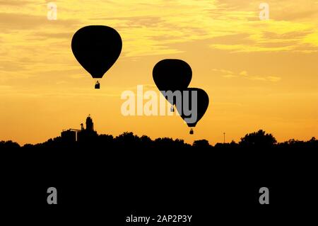 Trois montgolfières se profilent au coucher du soleil lorsque le flotteur au-dessus d'un paysage de l'Iowa. Banque D'Images