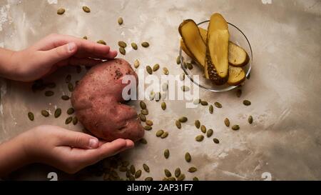 Nourriture laid, pommes de terre en forme de coeur.produits de ferme naturels et simples. Concombres salés fermentés. Graines de citrouille. Les mains des enfants tiennent Banque D'Images