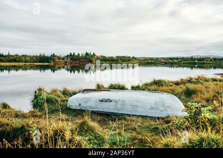 Vieux bateau inversé sur la côte pacifique avec de l'herbe verte du grand lac sous ciel nuageux Banque D'Images