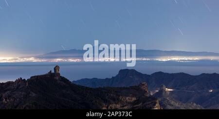 Vue de nuit de Gran Canaria vers Tenerife avec des sentiers étoilés au-dessus du volcan Teide et la côte illuminée, vu de la région autour de Roque Nublo. Banque D'Images