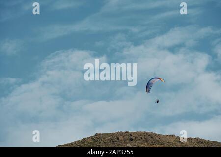 À partir de ci-dessous brave athlète méconnaissable avec parachute coloré plane au ciel bleu avec des nuages blancs moelleux et volant au-dessus d'atterrissage lentement hill Banque D'Images