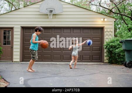 deux petits enfants pieds nus dribble ballons de basket dans une allée Banque D'Images