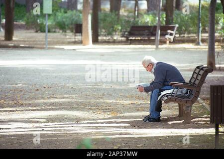 Albacete, Espagne, le 18 janvier 2020 : Senior homme assis sur un banc en bois, de lire le journal dans le parc Abelardo Sanchez Banque D'Images