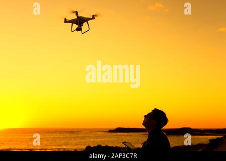 Une silhouette d'un homme à la recherche d'un drone dans le coucher du soleil. Banque D'Images