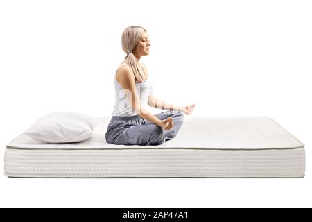 Jeune femme en pyjama assis sur un matelas de lit dans une pose de méditation isolé sur fond blanc Banque D'Images