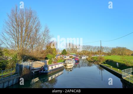 Long canal étroit bateaux amarrés sur un jour d'hiver ensoleillé, calme au bord de la rivière Nene en dehors de Northampton, en Angleterre. Banque D'Images