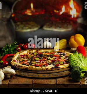 Pizza fraîche et faite à la main avec tomates rôties au four, poivrons, câpres, basilic et fromage rasé sur une planche en bois rustique Banque D'Images