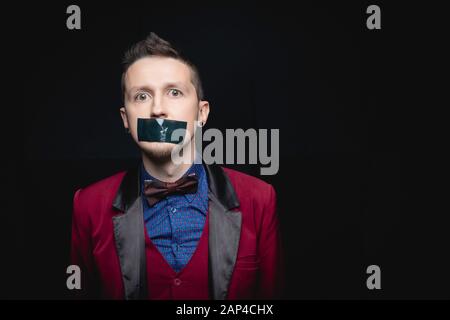 Homme en veste rouge avec ruban adhésif fermé sur sa bouche. Fond noir isolé Banque D'Images