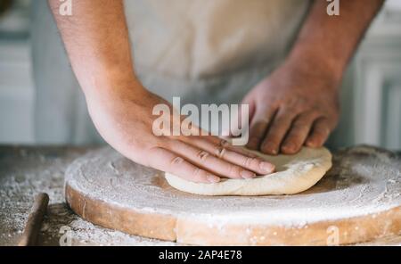 L'homme et de pétrissage de pâte à pizza maison de cuisson dans la cuisine. Gros plan sur les mains du boulanger la préparation du pain. La cuisson et la préparation des aliments à la maison. Banque D'Images