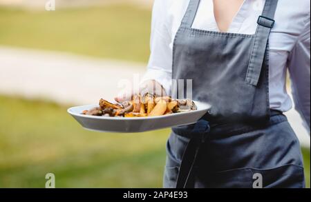 Service de restauration. L'homme de serveur dans le tablier porte des en-cas alimentaires sur le plateau Banque D'Images