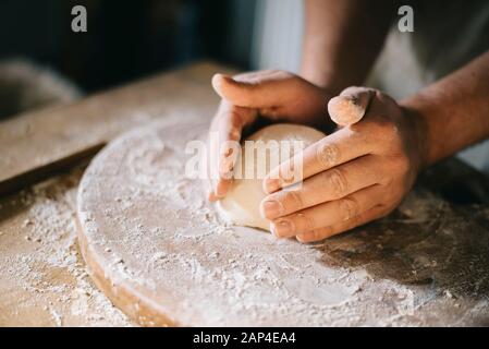 L'homme et de pétrissage de pâte à pizza maison de cuisson dans la cuisine. Gros plan sur les mains du boulanger la préparation du pain. La cuisson et la préparation des aliments à la maison. Banque D'Images