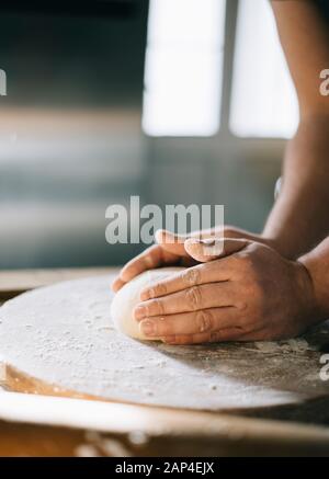 L'homme et de pétrissage de pâte à pizza maison de cuisson dans la cuisine. Gros plan sur les mains du boulanger la préparation du pain. La cuisson et la préparation des aliments à la maison. Banque D'Images